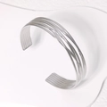 Brazalete abierto de plata multicapa con líneas geométricas sobre fondo de piedra blanca - Color Acero