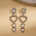Silver twisted heart drop earrings with rhinestones and black dots on a stone background - Silver