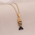 Golden fish necklace with black enamel scales and red gem eye on beige fabric background - Black