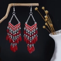 Dettaglio artistico di orecchini boho con nappe di perline rosse appesi a un ramo di legno - Stile Retrò con Perline Rosse (E6328) / Rosso