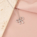 Vue détaillée du collier pendentif nœud argenté sur une pierre texturée et tissu rose doux - Style Nœud Papillon 9 (9#)