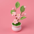 Handgehäkelte Blume im rosa Keramiktopf mit grünen Blättern auf rosa Hintergrund - Pfirsichblüte Topfpflanze / Rosa