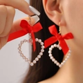 Sweet red ribbon bow earrings with heart pearl pendant shown on model and in hand - Red Satin Bowknot Artificial Pearl Heart Style (7809)
