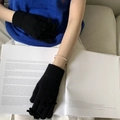 Close-up of black knitted gloves with bow detail worn by a model reading a book - One Size / Black