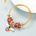 Gold wire bracelet featuring red rhinestone beads and a sparkling bee charm pendant - Red