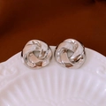Macro shot of silver polished love knot stud earrings on a white embossed ceramic plate - Shiny Silver Love Knot Stud Earrings