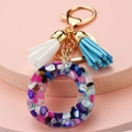 Detail of a resin keychain with colorful stones, gold hardware, and blue tassels - Letter O