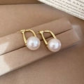 Detailed close-up of U-shaped gold earrings with large round white pearls on a velvet stand - Gold (Silver Earring Post)