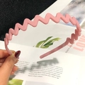 Close-up of a pink wavy matte headband held by hand with a stylish finish - Pink
