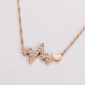 Detalle macro del collar de electrocardiograma oro rosa con colgante corazón y circonitas - Oro rosa