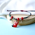 Detail of handmade braided Christmas bracelet with Santa sock charm and bell on wooden stand - Christmas Sock