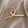 Close-up of a matte champagne gold metal hair claw clip on elegant silk background - Gold Cross