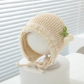 Detail der Baby-Strickhaube mit feiner Spitze und grünen gestrickten Blumenakzenten - 3-15 Monate / Beige
