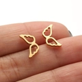 Macro view of gold angel wing stud earrings held between fingers showing hollow design - 672 Angel Wings / Gold