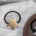 Close-up of golden brushed star charm on a high-elastic black hair tie over wooden base - Gold