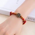 Gros plan d'un bracelet ethnique perlé avec perles rouges et charme émaillé sur le poignet - Grande Fortune