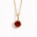 Primer plano del collar dorado con piedra de nacimiento y colgante de rubí rojo redondo - Enero Rojo Granate