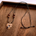 Détail macro du pendentif cœur ambre avec bord doré et étoiles vintage sur bois - Collier Cœur Ambre Cordon Noir (Café Clair)