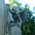 Grey resin gargoyle statue sculpture with wings climbing on a wooden garden fence - Gargoyle Sculpture