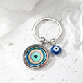 Detailed close-up of a blue Evil Eye glass pendant keychain on white textured stone background - Colorful Rainbow Eye