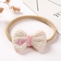 Détail d'un bandeau pour bébé avec nœud tricoté beige, dentelle rose et broderie d'étoile - Fil Beige