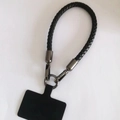 Detail van zwarte gevlochten leren polsband met metalen veersluiting en telefoonadapter - Gunmetal Gesp + Zwarte Band + Zwarte Patch