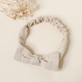 Close-up of beige muslin cotton baby headband with a soft bow and elastic texture - Beige