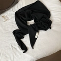 Detalle de chal de punto negro con etiqueta de marca sobre ropa de cama blanca - Negro