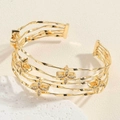 Detail van een gouden meerlaagse golvende open armband met sprankelende bloemaccenten - Bloem Armband SL0192-5