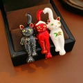 Detailed close-up of three enamel cat brooches with Christmas hats on black velvet - 38# Brooch - White - Red - Blue