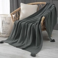 Dark grey chunky knit throw blanket with waffle texture and tassels on a wicker chair - Dark Gray