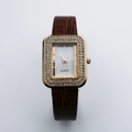 Close-up of square gold watch face with double crystal borders and brown leather strap - Coffee