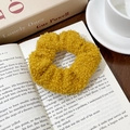 Détail d'un chouchou jaune en tissu pelucheux posé sur un livre ancien ouvert - Jaune gingembre