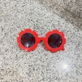 Detail shot of red flower-shaped kids' sunglasses with round lenses on a stone surface - Glossy China Red