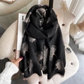 Black cashmere scarf with gold ginkgo leaf pattern and tassels on a cozy beige chair - Black