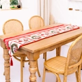 Camino de mesa navideño con borlas rojas y motivos de coronas sobre mesa de madera - Estilo Guirnalda de Navidad Roja