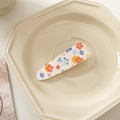 Detail of floral printed acrylic hair clip with colorful small blossoms on ceramic tray - White with Orange Flowers