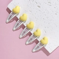 Detail showing five yellow heart hair clips on white metal bases over a pink surface - Yellow