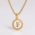 Detail of a golden round pendant with shell inlay featuring an embossed letter F on top - Letter F