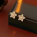 Dettaglio degli orecchini a stella dorati con micro-pavé di zirconi e finitura metallica - Oro