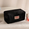 Detail of black plush makeup bag showing soft texture and woven motivational label - Black