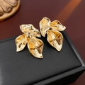 Primer plano de pendientes dorados en forma de pétalo sobre un estuche de cuero negro - Dorado / Dorado