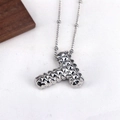 Macro detail of silver letter T pendant necklace with unique studded texture on white fabric - Letter T