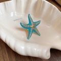 Macro shot of blue enamel starfish ring with gold accents in a shell dish - Blue