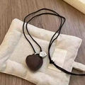 Detalle de colgante de corazón con cuerda trenzada negra y etiqueta de plata en bolsa - Collar-Marrón