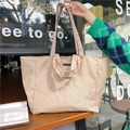 Detailaufnahme der Canvas-Tragetasche mit karierten Griffen und Logo auf dem Cafétisch - Khaki Kariert