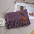 Solid purple cashmere-feel scarf with elegant fringes and leather brand tag on sofa - Taro Purple