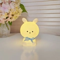 Cute bunny night light with blue plaid ribbon glowing in warm yellow ambient light - Big Head Rabbit - White - Blue
