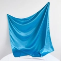 Detailed view of a glossy blue satin square scarf draped over an open book on a white surface - 90*90cm / Lake Blue