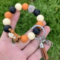 Close-up of silicone bead keychain bracelet with brown tassel and highland cow charm - Beige